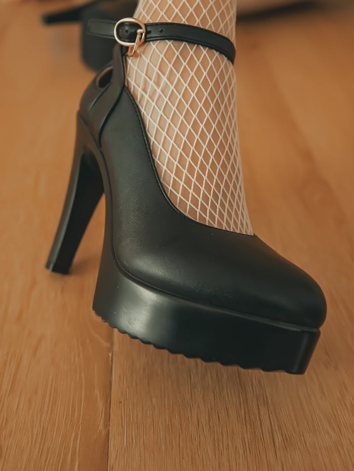 Fashionable black high heel with fishnet stocking on wooden floor - a chic footwear choice.